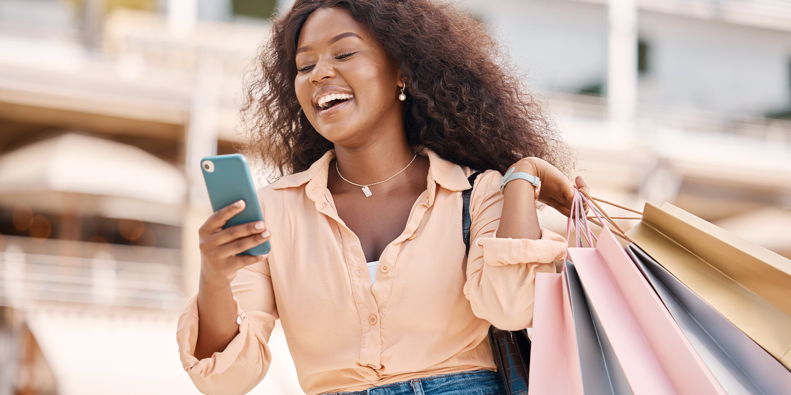 Fullgift. Une solution pour vos programmes cartes cadeaux. Gestion fluide des cartes cadeaux et physiques grâce à notre solution Numen. Image d'une femme souriante, dans un centre commercial, un téléphone dans sa main droite et des sacs de shopping dans sa main gauche.