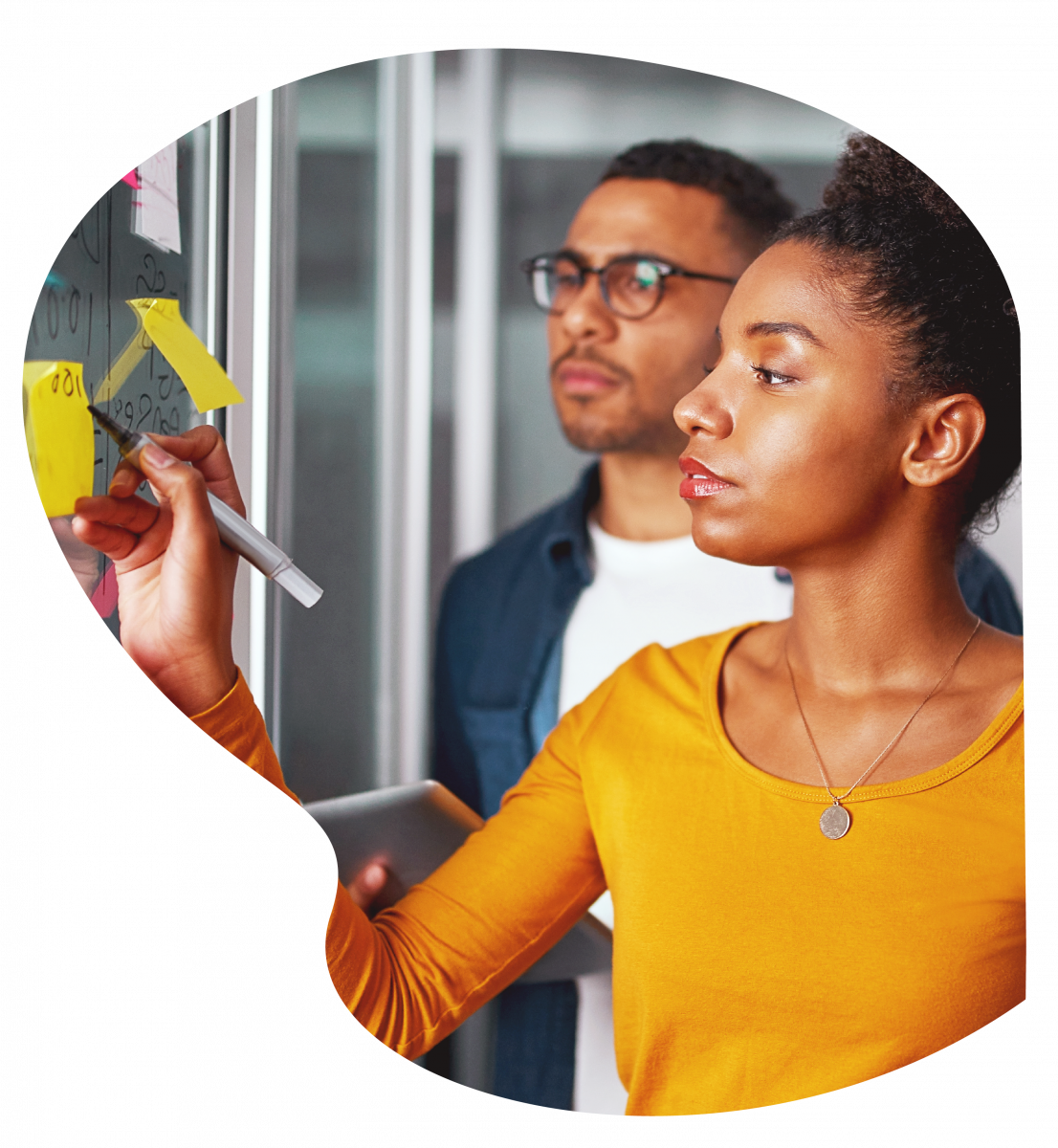 L'externalisation des processus métiers permet aux équipes de se recentrer sur des tâches à forte valeur ajoutée. Image d'un homme et d'une femme en plein brainstorming devant un tableau rempli de post-it. 